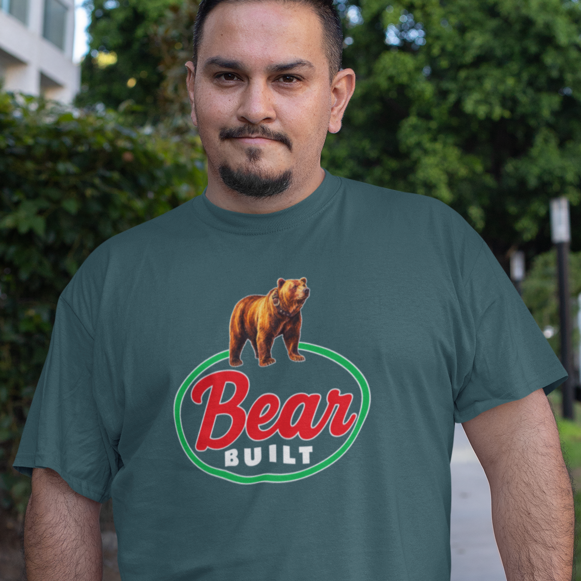 A man wearing a dark green graphic t-shirt with a 'Bear Built' logo and bear illustration, standing on an outdoor sidewalk.