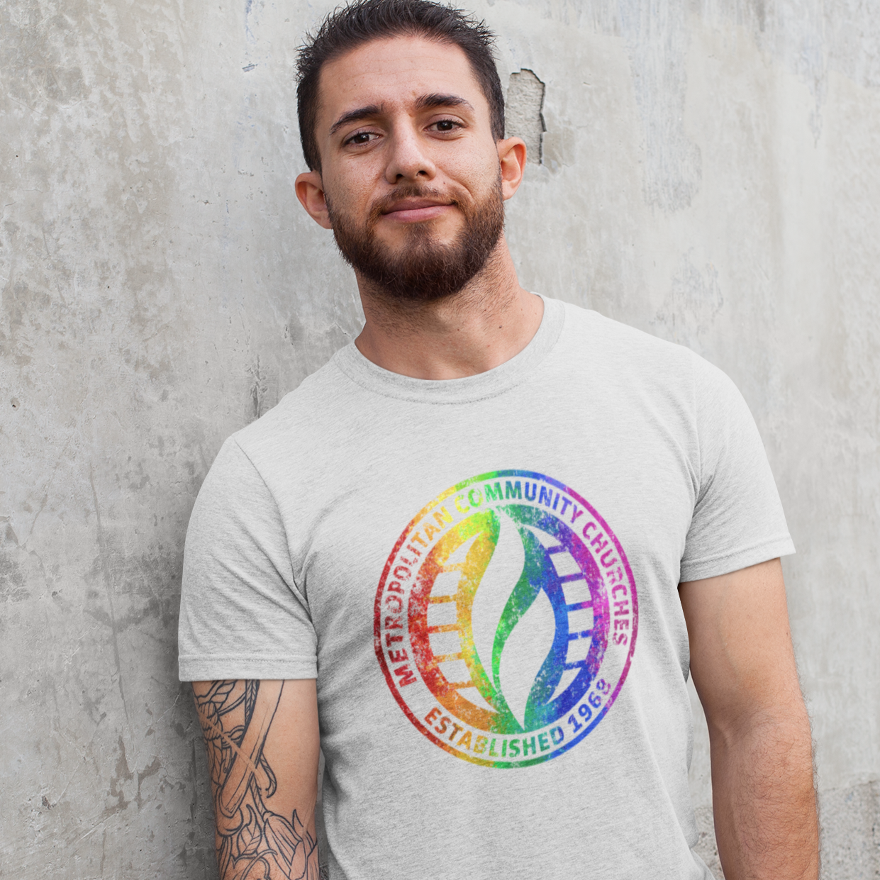 Man wearing a gray t-shirt with a colorful logo against a concrete wall.