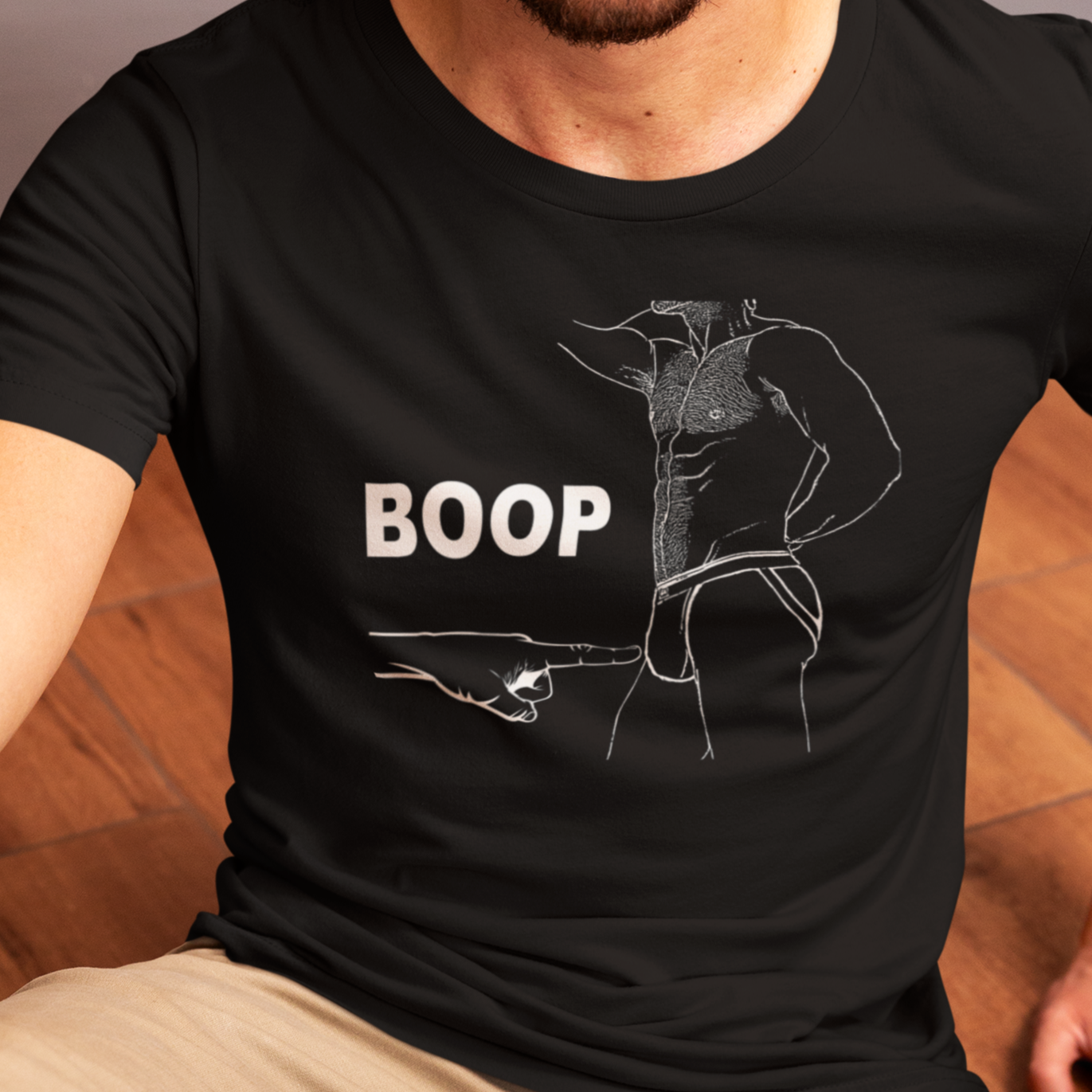 Man wearing a black t-shirt with 'BOOP' graphic design sitting on a wooden floor.